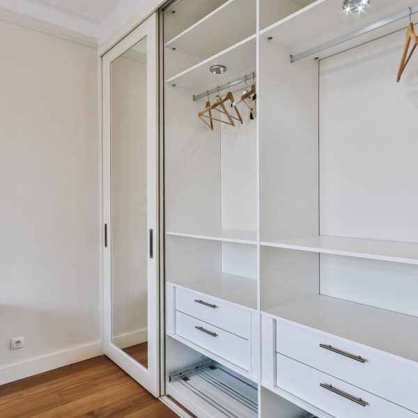 Minimalist white wardrobe with sliding mirror doors and wooden flooring in a modern bedroom.