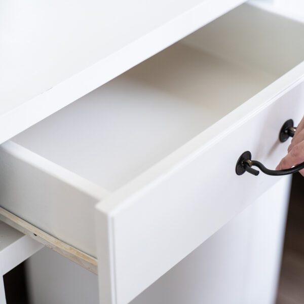 A person pulling open a white wooden drawer with black metal handles, showcasing the smooth sliding mechanism and classic design.