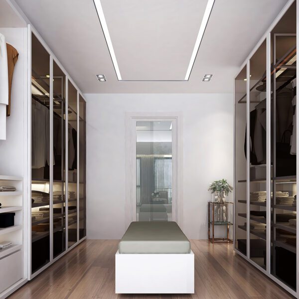 Modern walk-in closet with glass wardrobes, wooden flooring, and a white bench in the center.