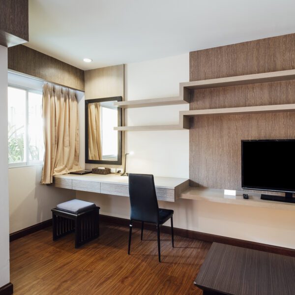 Stylish apartment living room featuring a modern TV cabinet with floating shelves, a built-in vanity desk, and a cozy workspace with natural lighting.