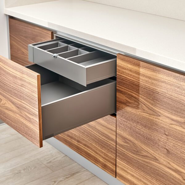 A modern kitchen with open walnut wood drawers featuring a sleek cutlery tray and an acrylic solid surface countertop.
